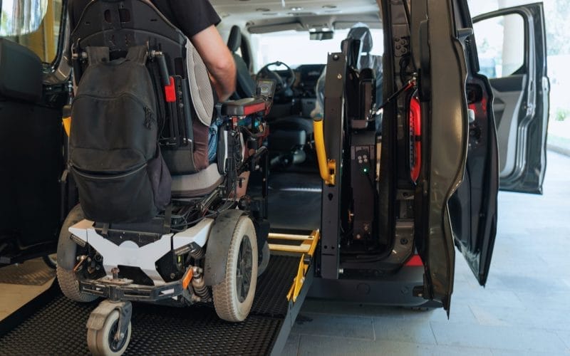 Disabled individual operating a lift on a rear-entry wheelchair van.