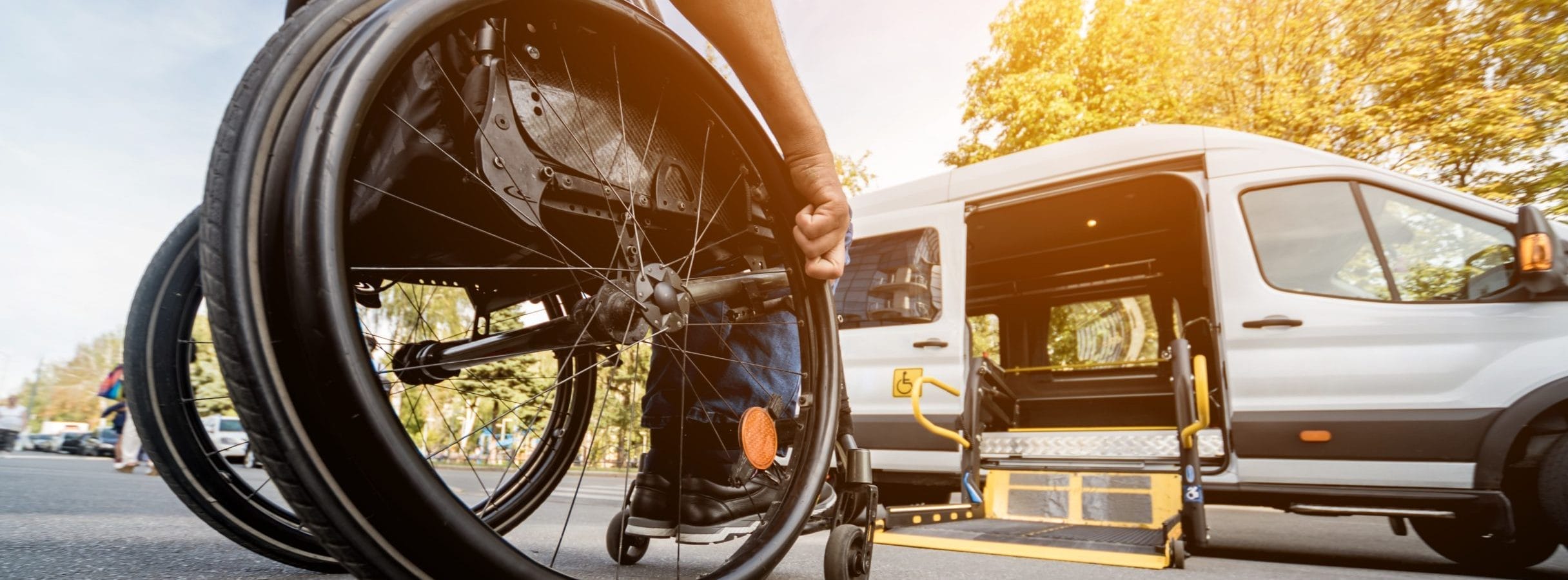 A man in a wheelchair moving toward an open side-entry lift on an ADA-accessible vehicle.
