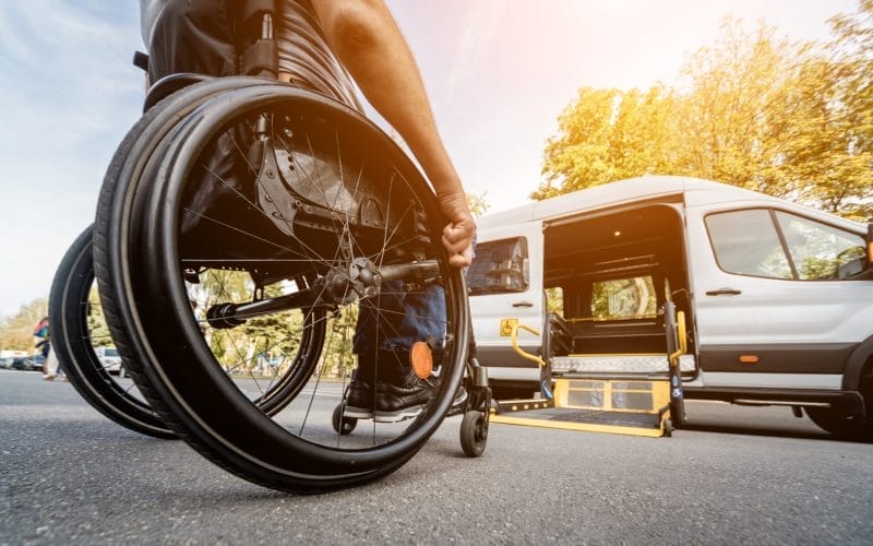 A man in a wheelchair moving toward an open side-entry lift on an ADA-accessible vehicle.