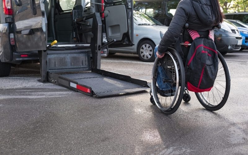 Person in a wheelchair going toward a lift on the back of an accessible vehicle to get in.